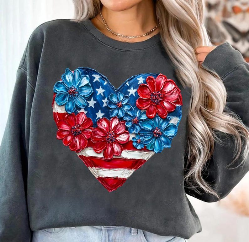 May include: A dark gray sweatshirt with a red, white, and blue heart-shaped design. The heart is made up of flowers with red, white, and blue petals. The design is reminiscent of the American flag.