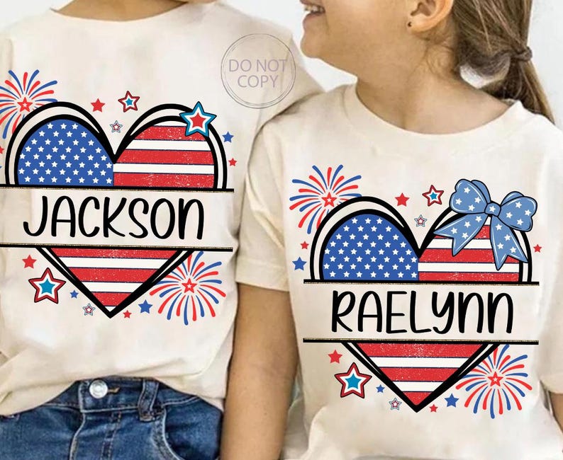 May include: Off-white t-shirts with patriotic heart designs. One shirt features the name "Jackson" and the other "Raelynn". The hearts are split into sections of blue stars and red and white stripes, with fireworks and star accents.