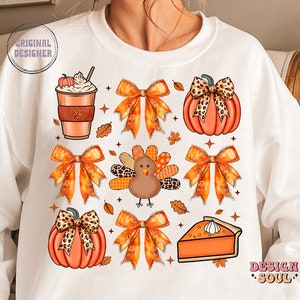 May include: White sweatshirt with a Thanksgiving theme featuring a pumpkin, a turkey, a pie, a coffee cup, and bows. The design is in orange, brown, and black.