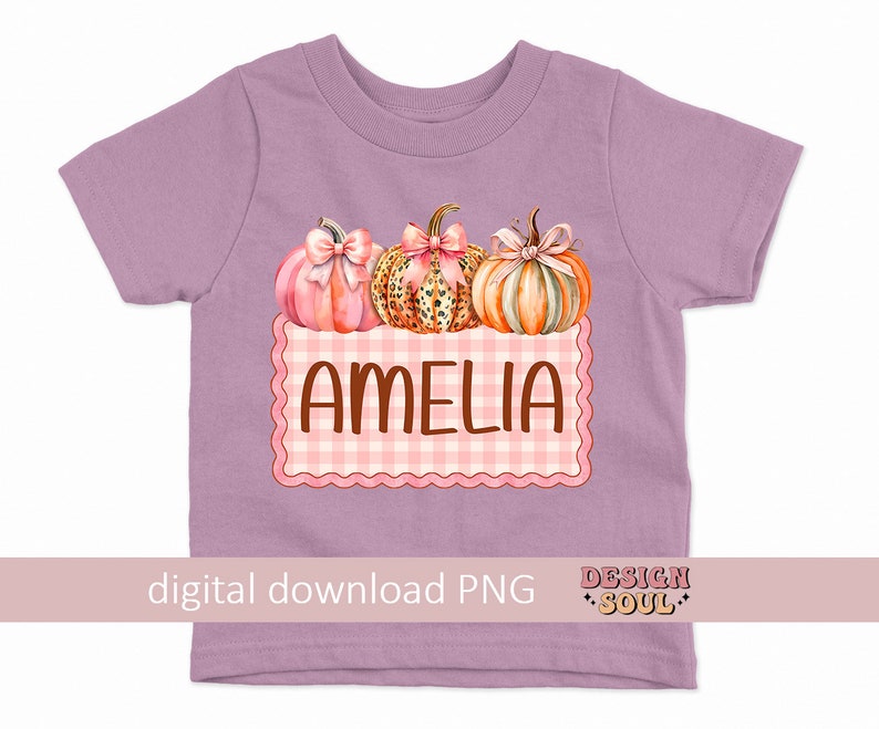 May include: A purple t-shirt with a pink and orange pumpkin design and the name Amelia in brown text on a pink and white checkered background.