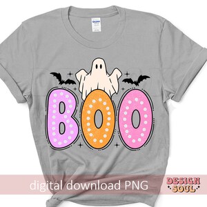 Op de afbeelding: Een grijs T-shirt met een spook en het woord "BOO" in roze en oranje stippen. De letters zijn zwart omrand. Boven het woord "BOO" bevinden zich twee zwarte vleermuizen.