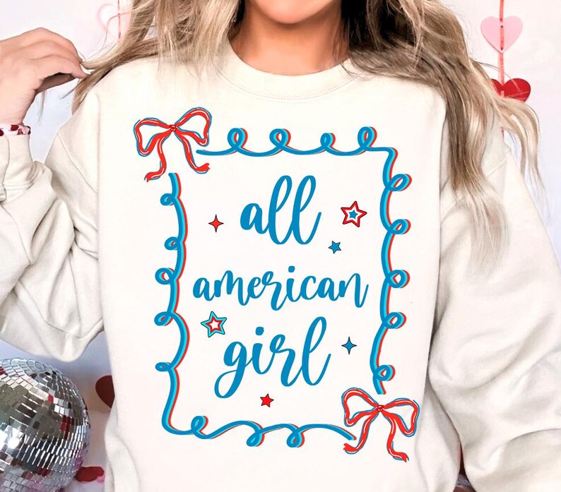 Peut inclure: Sweat-shirt blanc avec un motif graphique bleu et rouge qui dit "all american girl" avec des &eacute;toiles et des n&oelig;uds.