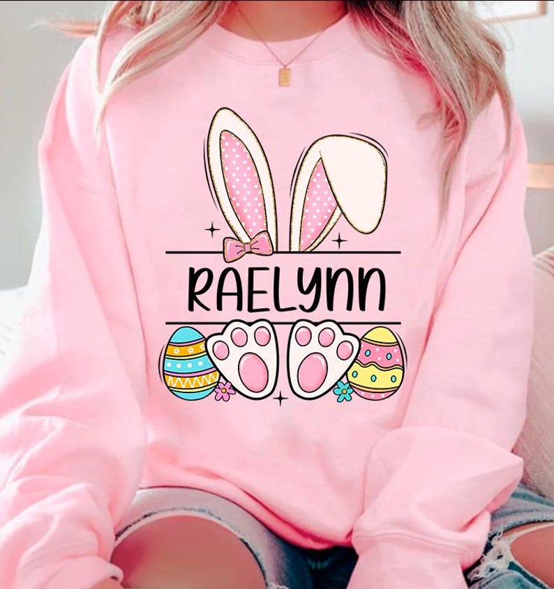 May include: Pink sweatshirt with a bunny ear design, Easter eggs, paw prints, and the name "RAELynn" printed on the front.