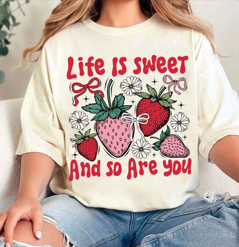 May include: A white t-shirt with a red graphic that says "Life is sweet and so are you". The graphic also features strawberries and flowers.