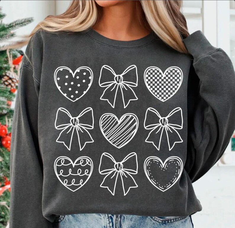 May include: A charcoal gray sweatshirt with a white design of nine hearts and bows. The hearts are filled with different patterns, including polka dots, checkered, and stripes.