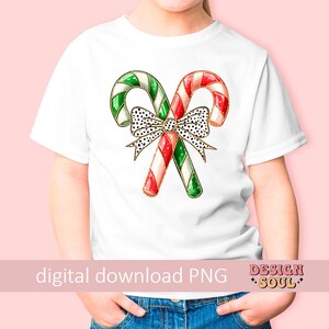 May include: White t-shirt with a red and green candy cane design and a black and white polka dot bow. The candy canes are decorated with gold glitter.