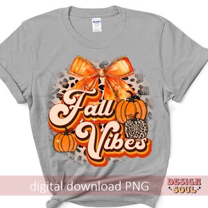 May include: A gray t-shirt with a graphic design featuring a large orange bow, pumpkins, and the text "Fall Vibes" in a retro font.
