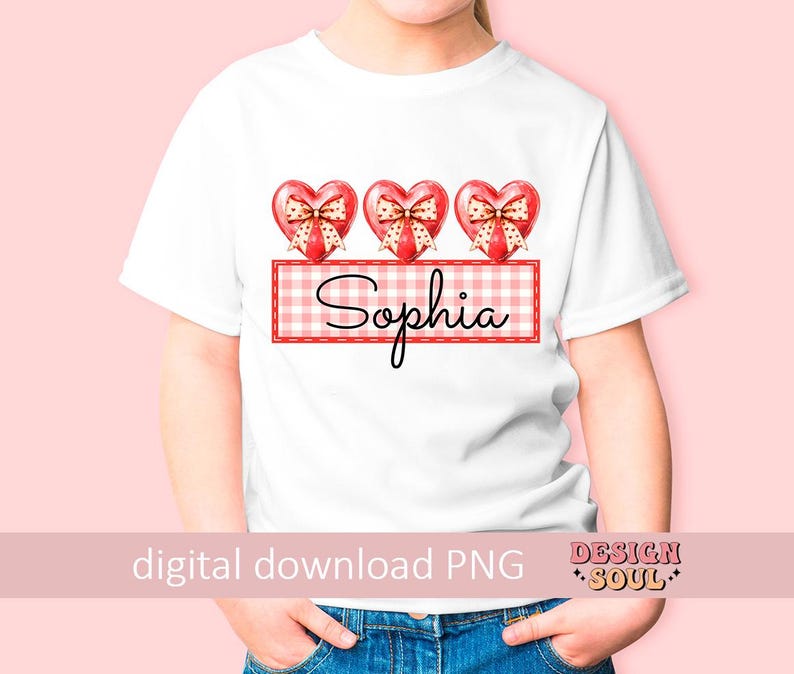 May include: White t-shirt with three red hearts with bows and a red and white gingham banner with the name "Sophia" printed on it.