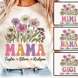 May include: Cream-colored t-shirt featuring a floral design with daisies in shades of purple, pink, and white. The word "MAMA" is printed in retro-style letters. Additional designs include "MIMI", "NANA", and "GIGI" with names below.