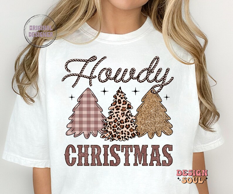 May include: White t-shirt with the text "Howdy Christmas" in brown lettering. The text is surrounded by three Christmas trees, one with a plaid pattern, one with a leopard print, and one with gold glitter.