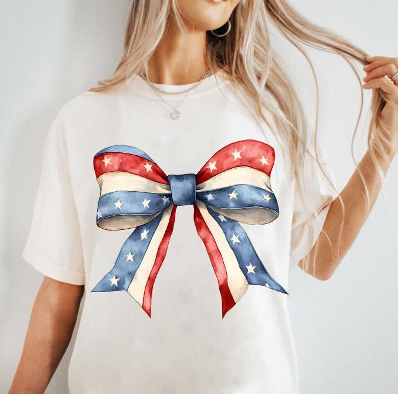 K&ouml;nnte beinhalten: Ein wei&szlig;es T-Shirt mit einer rot-wei&szlig;-blauen Schleife, die auf der Vorderseite aufgedruckt ist. Die Schleife besteht aus Stoff mit wei&szlig;en Sternen auf blauem Hintergrund. Die Schleife ist zu einem Knoten gebunden und die Enden schweben.