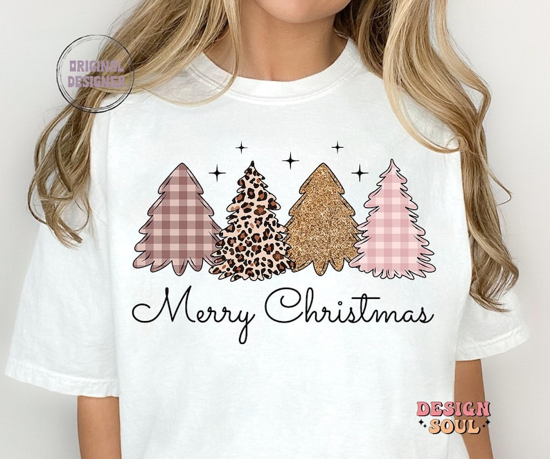 May include: White t-shirt with a graphic of three Christmas trees. The trees are decorated with pink and white gingham, leopard print, and gold glitter. The text "Merry Christmas" is printed below the trees.