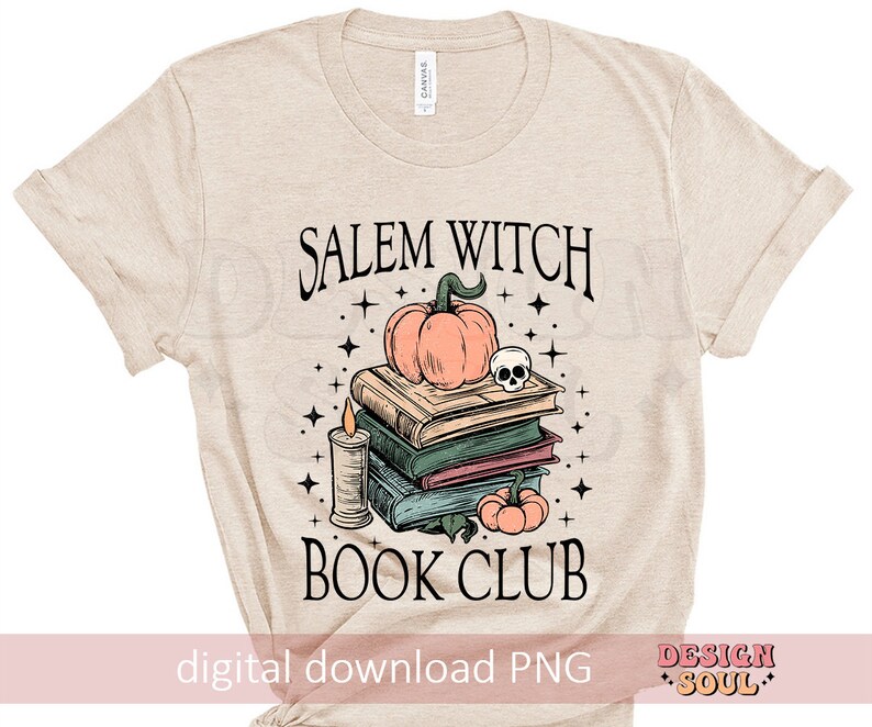 Op de afbeelding: Een beige T-shirt met de tekst "Salem Witch Book Club" gedrukt op de voorkant. Het ontwerp bevat een stapel boeken, een pompoen, een schedel en een kaars.
