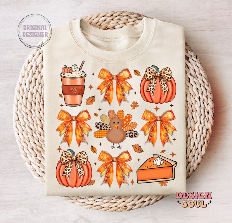 May include: A beige sweatshirt with a Thanksgiving-themed design featuring a turkey, pumpkins, bows, a slice of pie, and a cup of coffee. The design is in shades of orange, brown, and white.