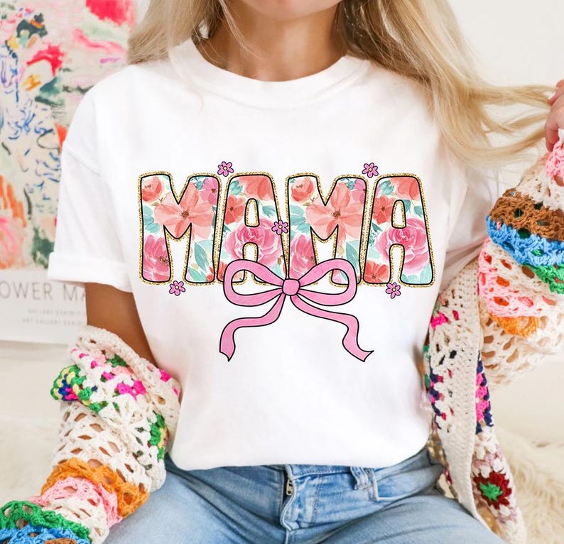 May include: White t-shirt with a floral design that spells out "MAMA" with a pink bow in the center.