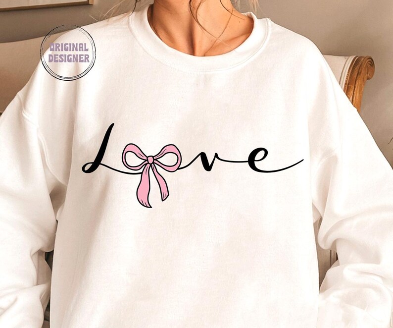May include: White sweatshirt with the word "Love" written in black cursive with a pink bow in the middle of the word.