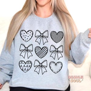 May include: A gray sweatshirt with a black design of hearts and bows. The design is repeated nine times on the front of the sweatshirt.