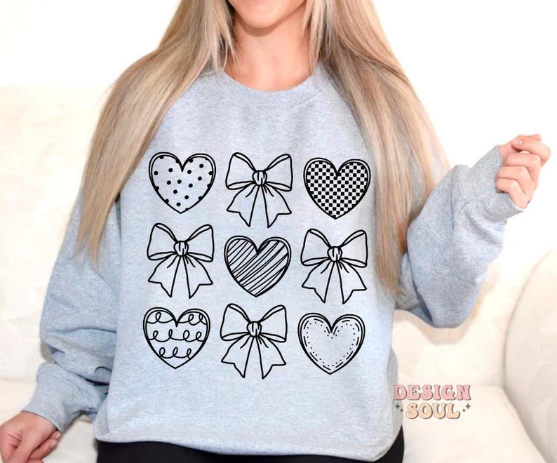 May include: A gray sweatshirt with a black design of hearts and bows. The design is repeated nine times on the front of the sweatshirt.