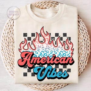 May include: A cream-colored sweatshirt with a graphic design of a flame with a leopard print pattern. The text "American Vibes" is in a retro font with red and blue accents. The background is a black and white checkered pattern.