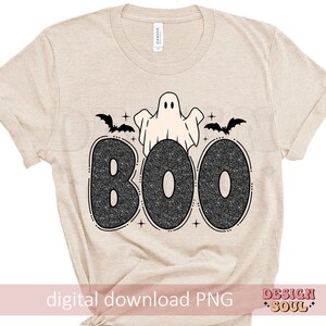 May include: A beige t-shirt with a black and white graphic of a ghost and bats with the word "BOO" in sparkly letters.
