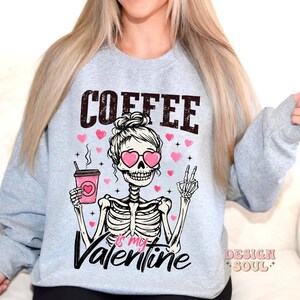 May include: Gray sweatshirt with a skeleton holding a coffee cup and wearing heart-shaped sunglasses. The text on the sweatshirt reads "Coffee is my Valentine".