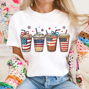 May include: White t-shirt with a graphic of four iced coffee drinks decorated with red, white, and blue stars and stripes.