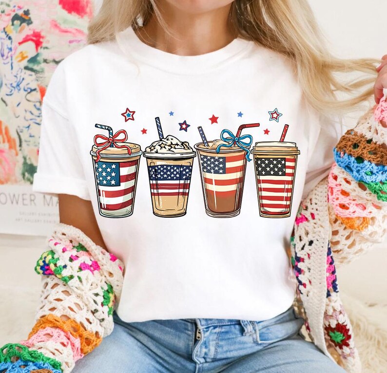May include: White t-shirt with a graphic of four iced coffee drinks decorated with red, white, and blue stars and stripes.