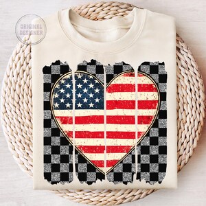 May include: A cream-colored sweatshirt with a distressed, glittery checkered background and a heart-shaped American flag design.