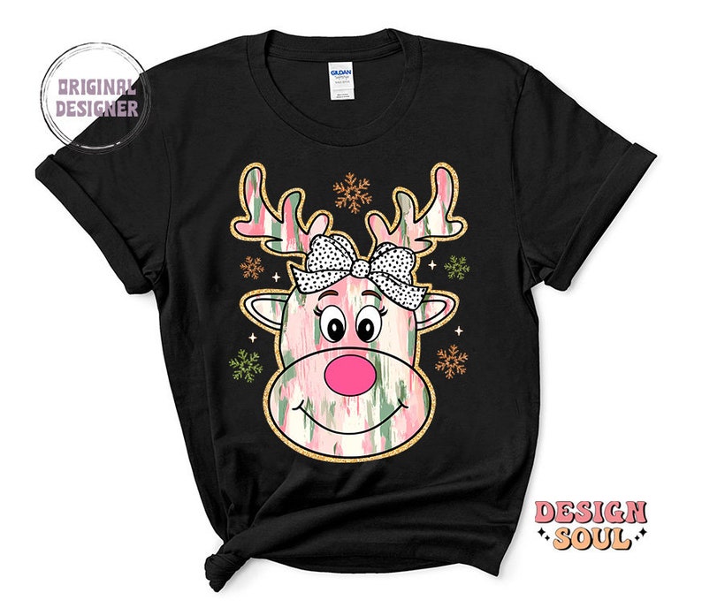May include: Black t-shirt with a pink and green reindeer face graphic. The reindeer has a pink nose and a pink bow with white polka dots. The graphic is surrounded by snowflakes.