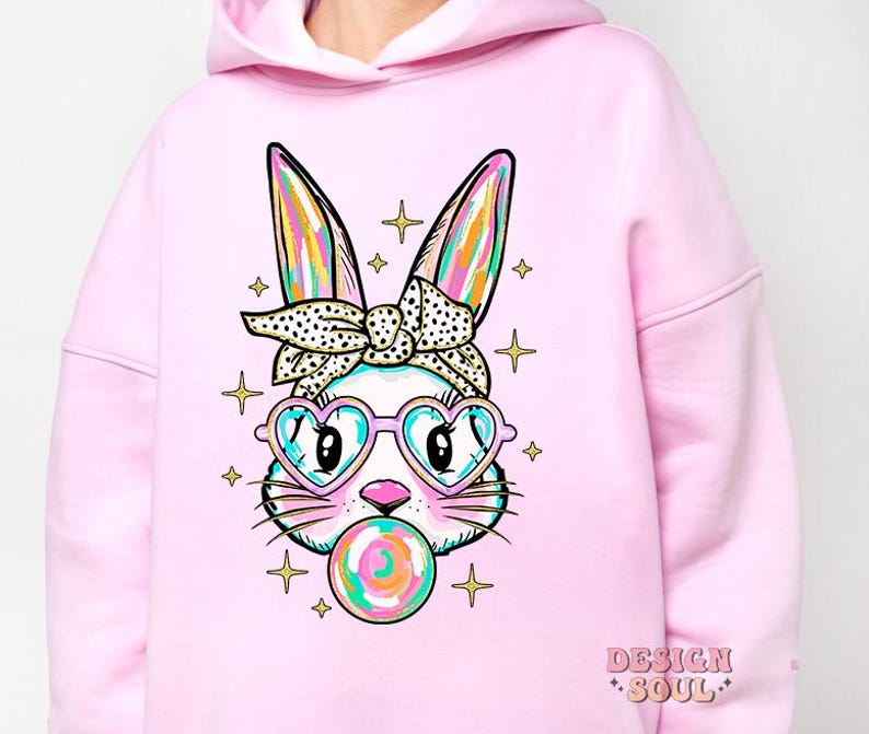 May include: Pink hoodie with a graphic of a cartoon bunny wearing sunglasses and a headband. The bunny is holding a colorful lollipop. The hoodie has the text "DESIGN SOUL" on the bottom right corner.