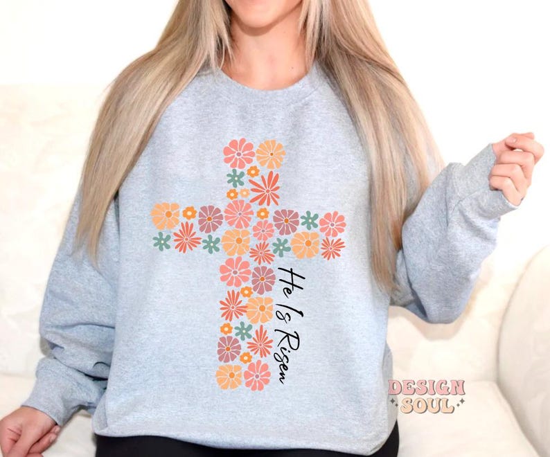 May include: A light gray sweatshirt with a floral cross design and the text "He is Risen".
