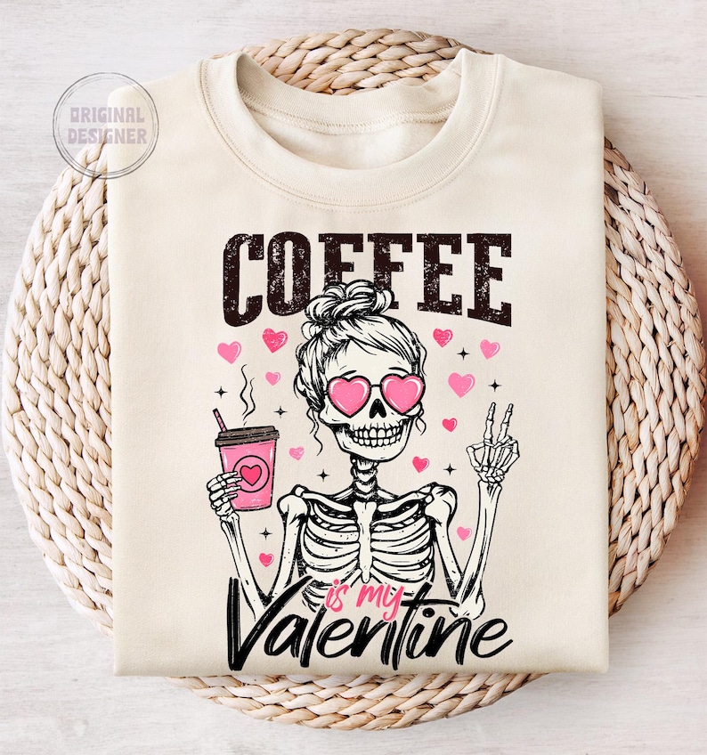 May include: A beige sweatshirt with the text "COFFEE is my VALENTINE" in black. A cartoon skeleton wearing pink sunglasses and a bun holds a pink and white coffee cup. Pink hearts are scattered around the skeleton.