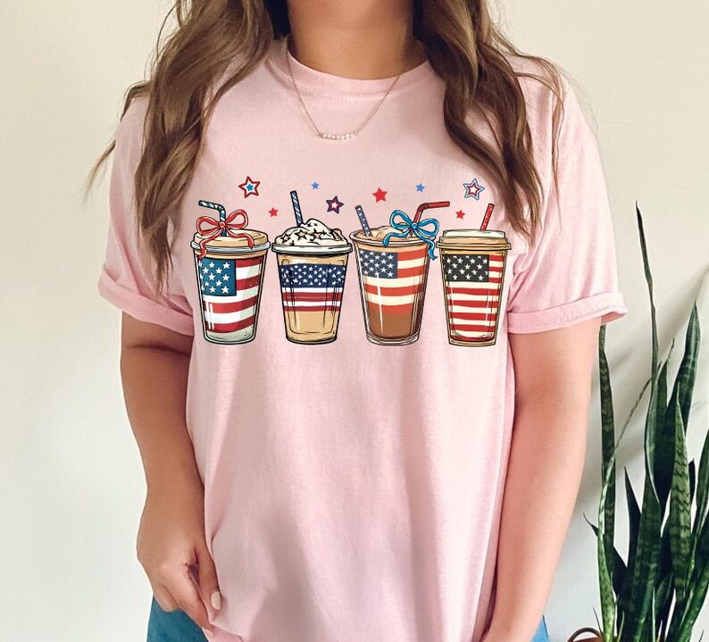 May include: Pink t-shirt with a graphic of four iced coffee cups decorated with the American flag.