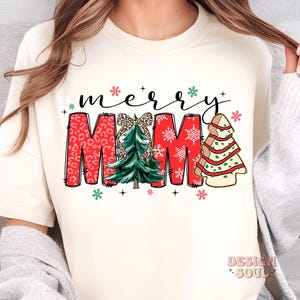 May include: White t-shirt with a red "Merry Mama" design featuring a Christmas tree with a bow, snowflakes, and a gingerbread tree.