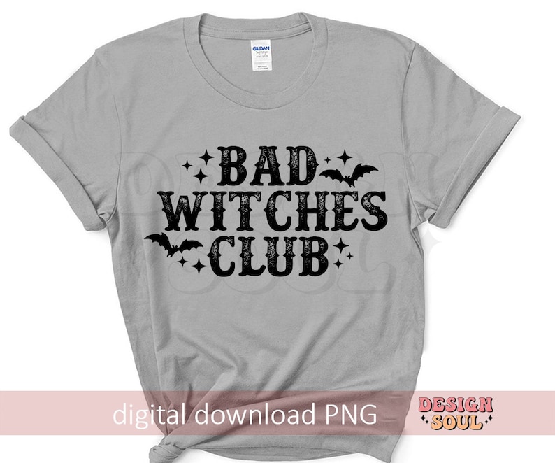 May include: A light gray t-shirt with the words "BAD WITCHES CLUB" in black, gothic-style lettering. The design includes bats and stars. The shirt is a Gildan brand.