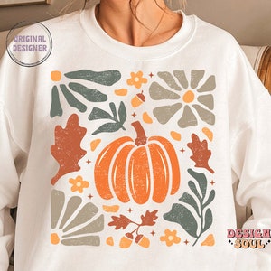 May include: White sweatshirt featuring a graphic design of a pumpkin and autumn foliage in shades of orange, brown, and green. The design is in a square shape and has a vintage aesthetic.