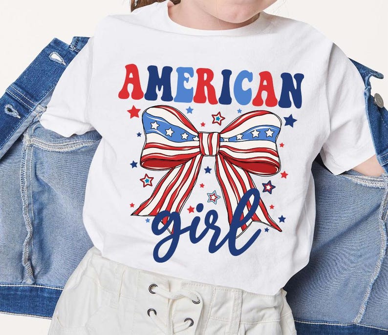 May include: White t-shirt with a red, white, and blue bow with stars and the text "AMERICAN girl" in blue.
