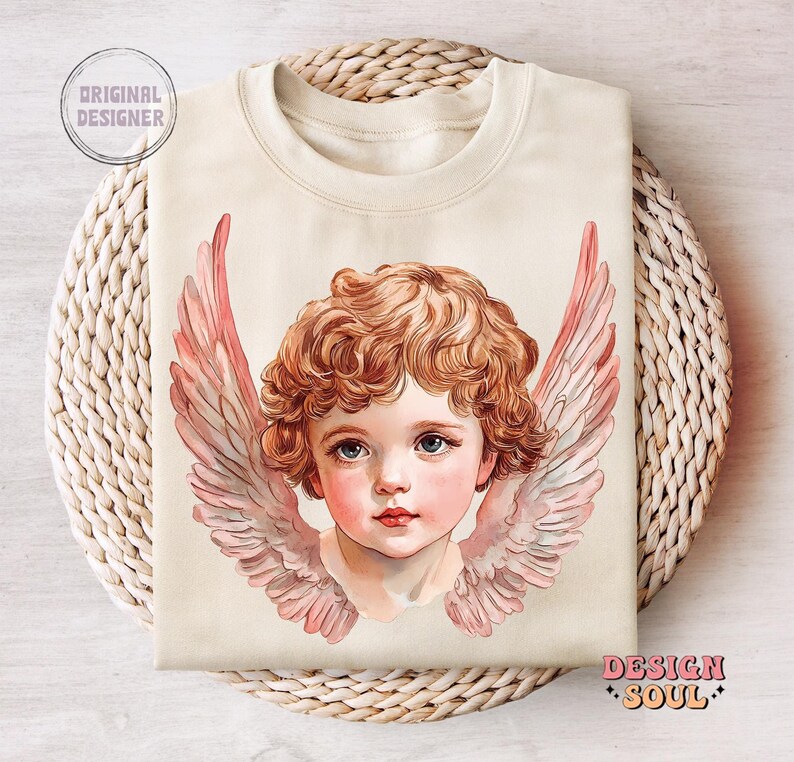 Op de afbeelding: Een cr&egrave;mekleurige trui met een vintage-illustratie van een cherubijn met roze vleugels. De cherubijn heeft krullend blond haar en draagt een witte kleding.