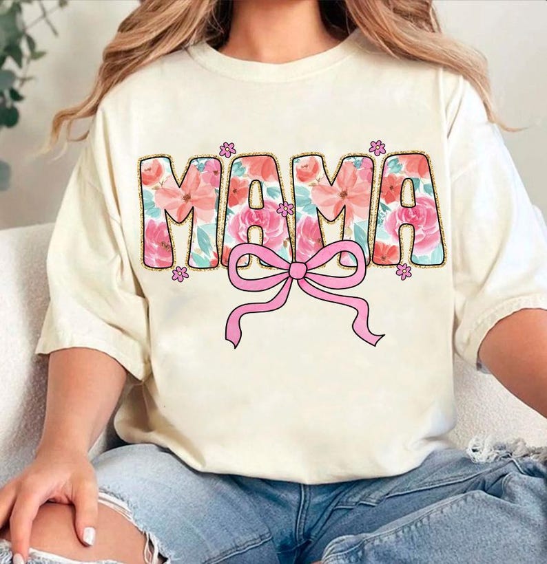 May include: A white t-shirt with a floral design that spells out "MAMA" with a pink bow underneath.