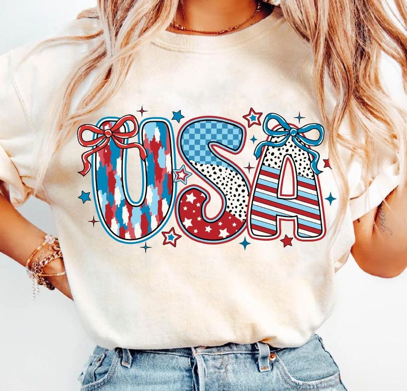 May include: A white t-shirt with a red, white, and blue "USA" graphic. The letters are decorated with different patterns, including stars, stripes, and polka dots.