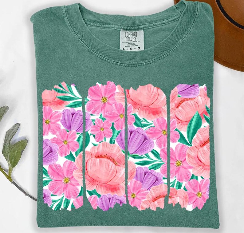 May include: A teal green t-shirt with a floral print design. The print features pink, purple, and green flowers. The shirt has a crew neck and short sleeves.