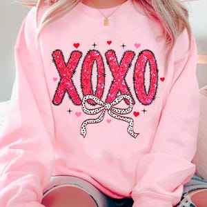 May include: Pink sweatshirt with a pink and black XOXO design with a bow and hearts.