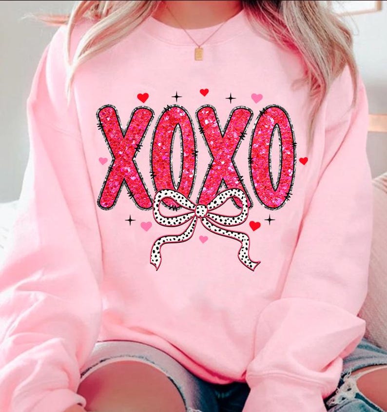 May include: Pink sweatshirt with a pink and black XOXO design with a bow and hearts.