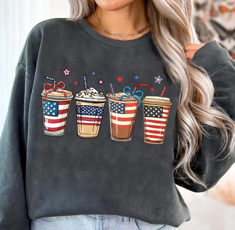 May include: A dark gray sweatshirt with a graphic of four iced coffee cups decorated with the American flag. Each cup has a straw and a red, white, and blue ribbon.