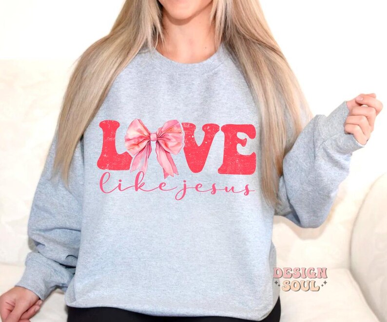 May include: A grey sweatshirt with the words "LOVE like jesus" printed in pink and red. A pink bow is in the middle of the word "LOVE".