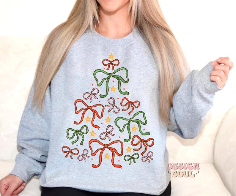 May include: A grey sweatshirt with a Christmas tree design made of colourful bows and stars. The tree is centred on the front of the sweatshirt.