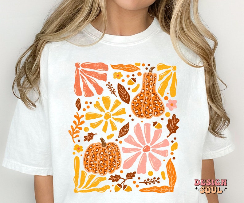 May include: White t-shirt with a graphic print of orange, yellow, pink, and brown pumpkins and flowers. The text "DESIGN SOUL" is printed in the bottom right corner.