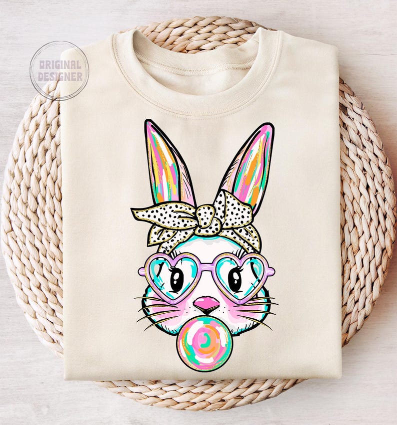 May include: A white sweatshirt featuring a colourful bunny rabbit wearing heart-shaped sunglasses and a polka dot bow. The bunny is holding a colourful lollipop.