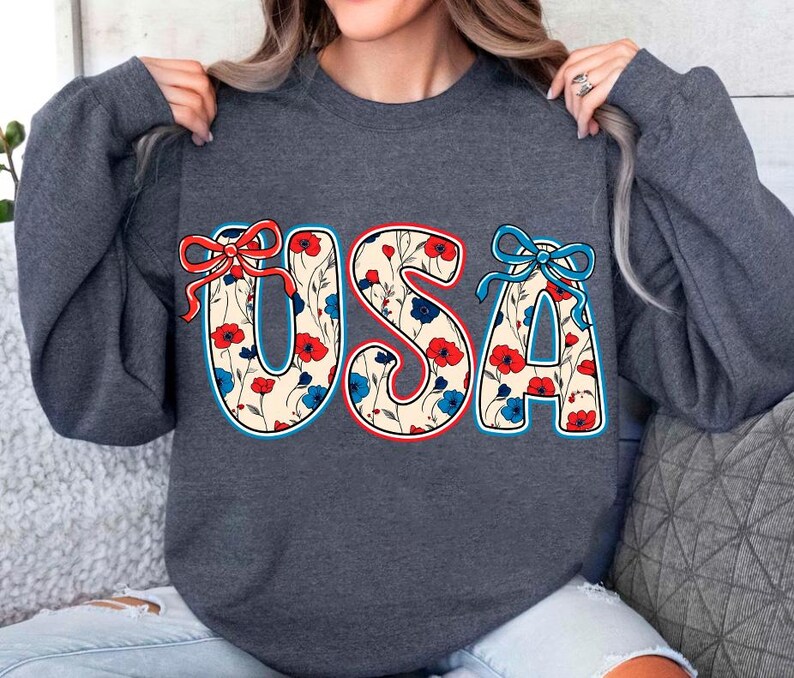 May include: A dark gray sweatshirt with a floral pattern "USA" graphic. The letters are outlined in blue and red, and the flowers are red, blue, and white.
