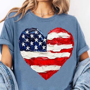 Pu&ograve; includere: Una maglietta blu con una bandiera americana dipinta a forma di cuore.